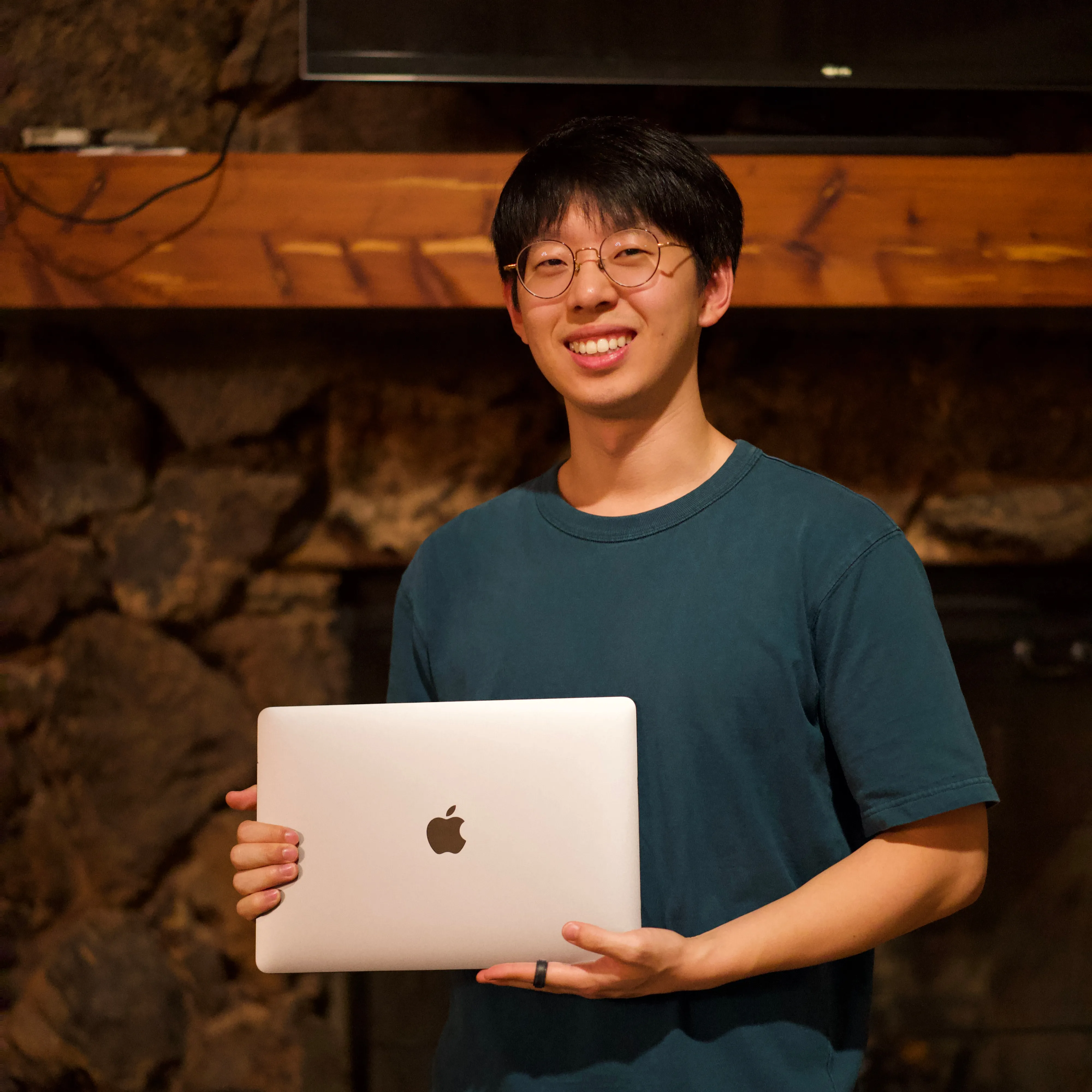 Jason Hwang holding a Macbook Pro, smiling at the camera. He's wearing his a green Uniqlo T-shirt.